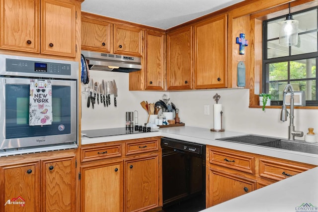 kitchen featuring brown cabinets, under cabinet range hood, light countertops, a sink, and black appliances