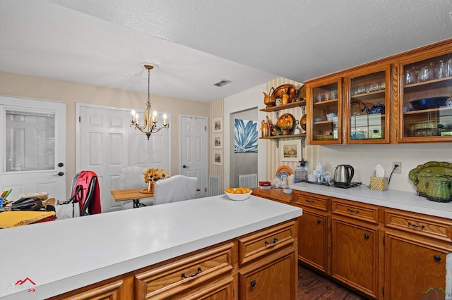 kitchen with brown cabinetry, light countertops, visible vents, and an inviting chandelier