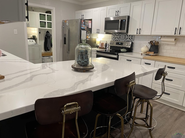 kitchen with white cabinetry, stainless steel appliances, light stone counters, crown molding, and a kitchen bar