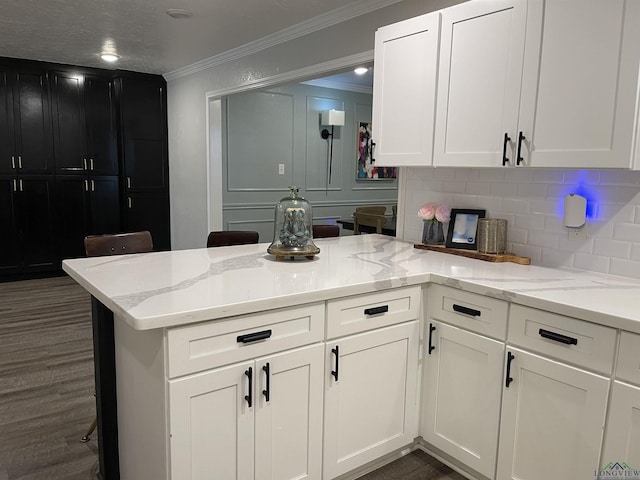 kitchen with white cabinetry, tasteful backsplash, light stone counters, kitchen peninsula, and ornamental molding