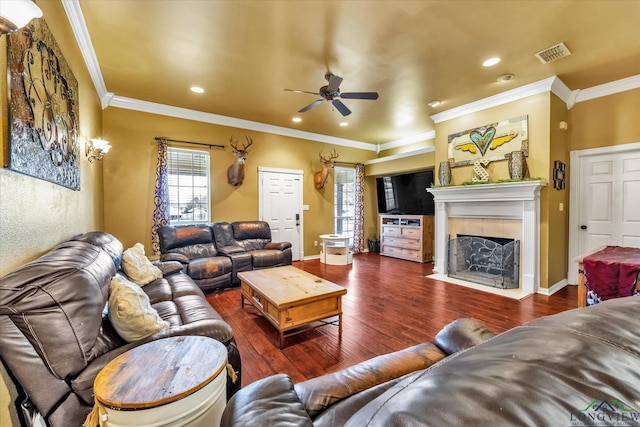 living room with a tiled fireplace, dark hardwood / wood-style flooring, ornamental molding, and ceiling fan