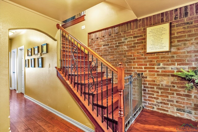 stairway with brick wall and hardwood / wood-style flooring