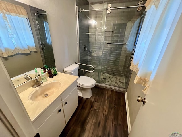 bathroom featuring toilet, a stall shower, wood finished floors, and vanity