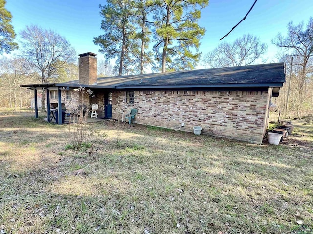 back of property with a chimney, a lawn, and brick siding