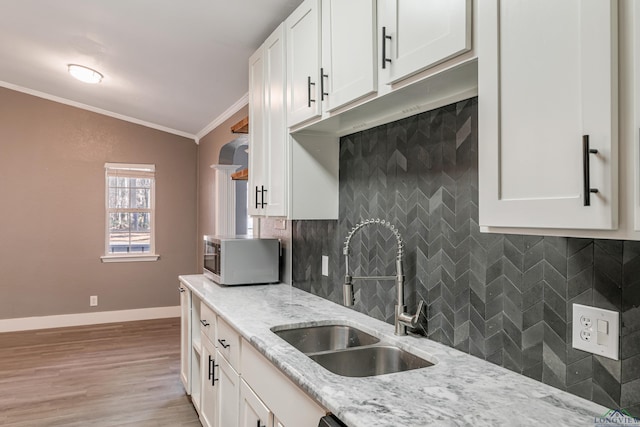 kitchen with light stone counters, crown molding, white cabinetry, and sink