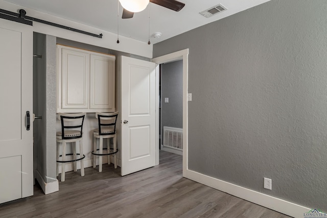 unfurnished bedroom with a barn door, ceiling fan, and hardwood / wood-style floors