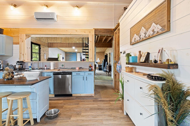 kitchen with stainless steel dishwasher, a wall mounted AC, wooden walls, a breakfast bar, and light wood-type flooring