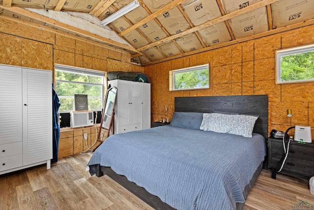 bedroom featuring multiple windows, wooden walls, and light hardwood / wood-style floors