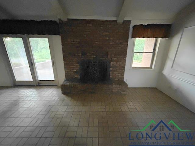 unfurnished living room featuring beamed ceiling, a brick fireplace, and plenty of natural light