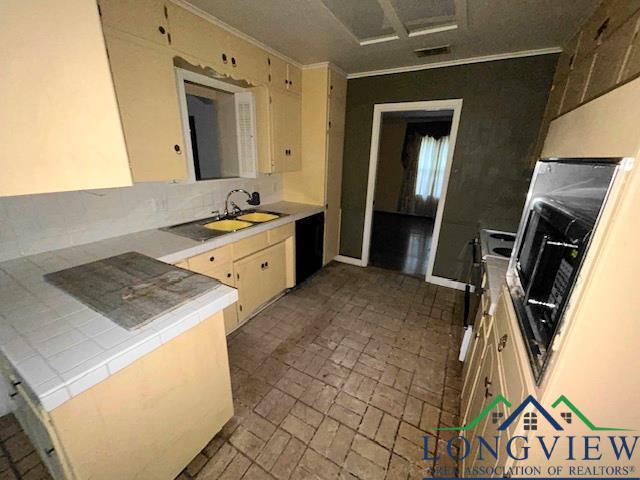 kitchen with stove, tasteful backsplash, ornamental molding, sink, and cream cabinetry