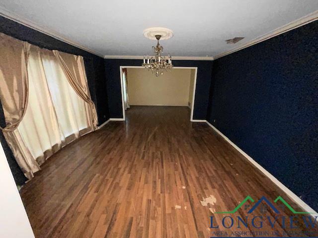 empty room featuring ornamental molding, dark wood-type flooring, and a notable chandelier