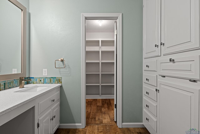 bathroom with a textured ceiling, wood finished floors, vanity, baseboards, and a spacious closet