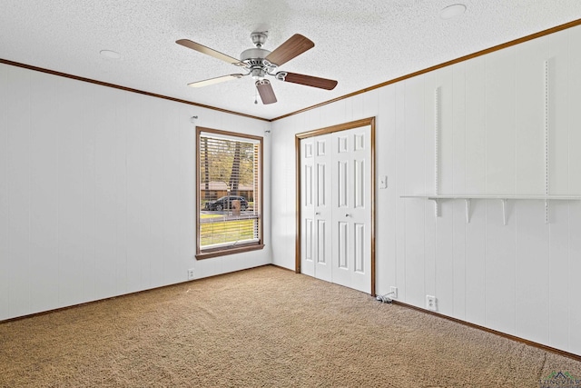 unfurnished bedroom with ornamental molding, a textured ceiling, a closet, carpet floors, and ceiling fan