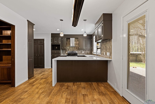 kitchen featuring a peninsula, a sink, light countertops, range with electric stovetop, and wall chimney range hood
