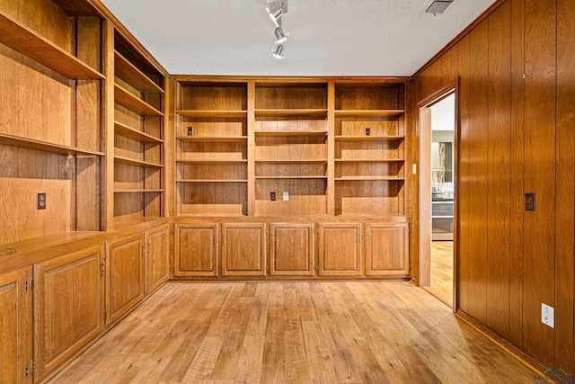 interior space featuring visible vents, wood walls, a textured ceiling, and light wood-type flooring