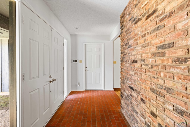 hallway with brick wall, a textured ceiling, baseboards, and brick floor