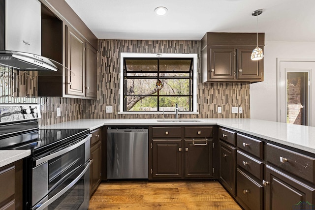 kitchen with a sink, tasteful backsplash, stainless steel appliances, dark brown cabinetry, and wall chimney range hood