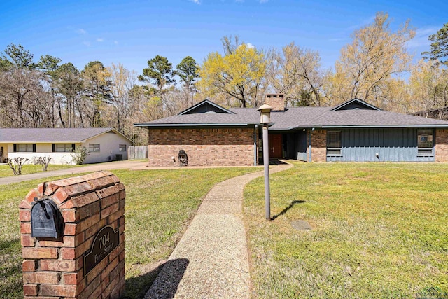 ranch-style house with board and batten siding, a front yard, a shingled roof, brick siding, and a chimney