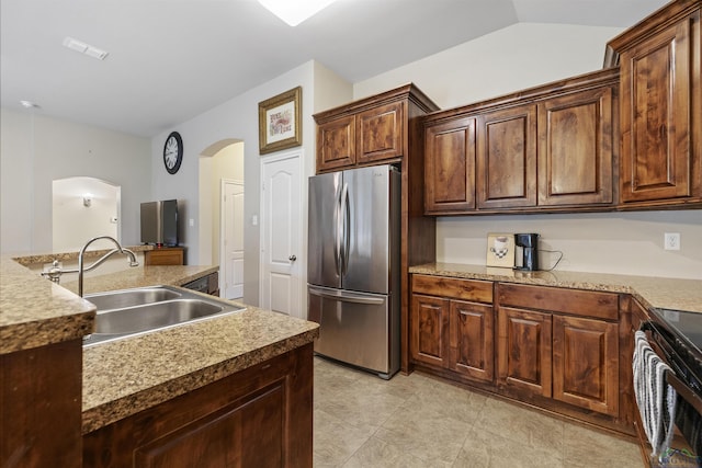 kitchen with visible vents, a sink, arched walkways, freestanding refrigerator, and black electric range