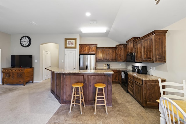 kitchen featuring arched walkways, vaulted ceiling, a breakfast bar, a kitchen island, and black appliances