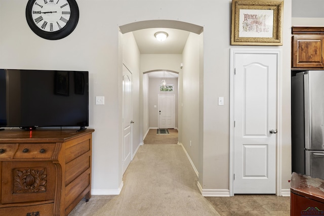 hall with baseboards, arched walkways, and light colored carpet
