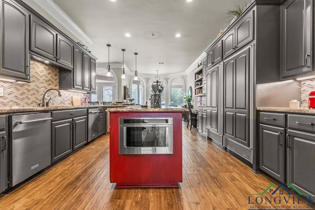 kitchen featuring stainless steel appliances, hanging light fixtures, a kitchen island, light stone countertops, and plenty of natural light