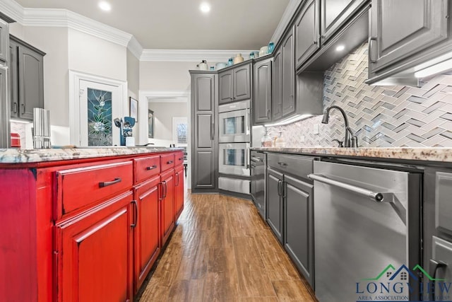 kitchen with appliances with stainless steel finishes, gray cabinetry, crown molding, dark wood-type flooring, and tasteful backsplash