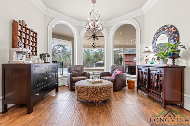 sitting room with ornamental molding, hardwood / wood-style floors, and ceiling fan with notable chandelier