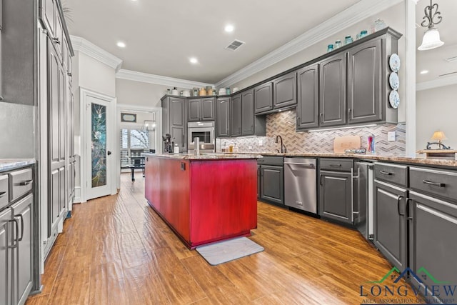 kitchen featuring appliances with stainless steel finishes, light stone counters, ornamental molding, and decorative light fixtures