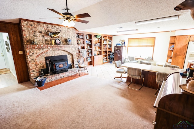 carpeted living room featuring a textured ceiling, a wood stove, ceiling fan, and wooden walls