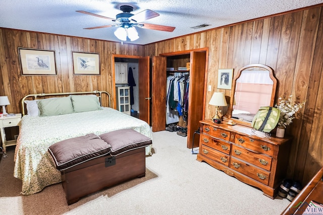 bedroom with ceiling fan, light colored carpet, a textured ceiling, wooden walls, and a closet