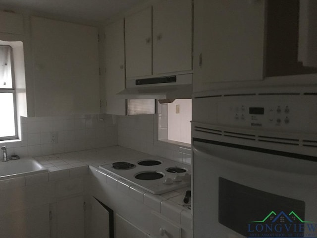 kitchen with white cabinets, tile counters, white appliances, and sink