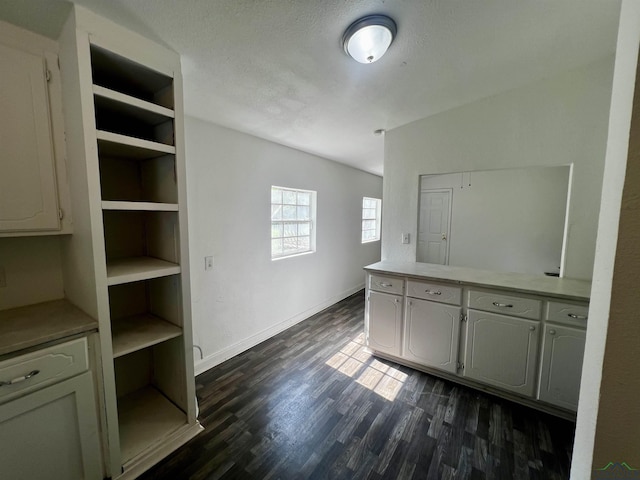 interior space with a textured ceiling, built in features, white cabinets, and dark hardwood / wood-style floors