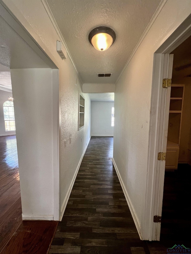 corridor featuring built in features, dark hardwood / wood-style floors, a textured ceiling, and ornamental molding