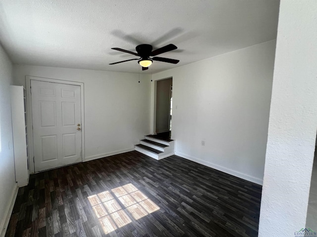 empty room featuring ceiling fan, dark wood-type flooring, and a textured ceiling