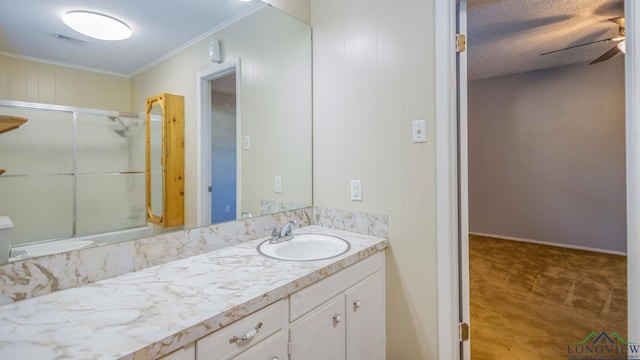 bathroom with vanity, ceiling fan, ornamental molding, a textured ceiling, and a shower with shower door