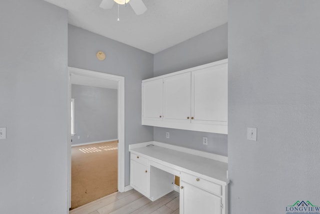 office space with light wood-style floors, ceiling fan, built in desk, and baseboards