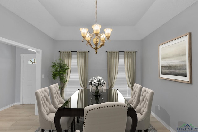 dining room featuring a notable chandelier, a tray ceiling, light wood finished floors, and baseboards