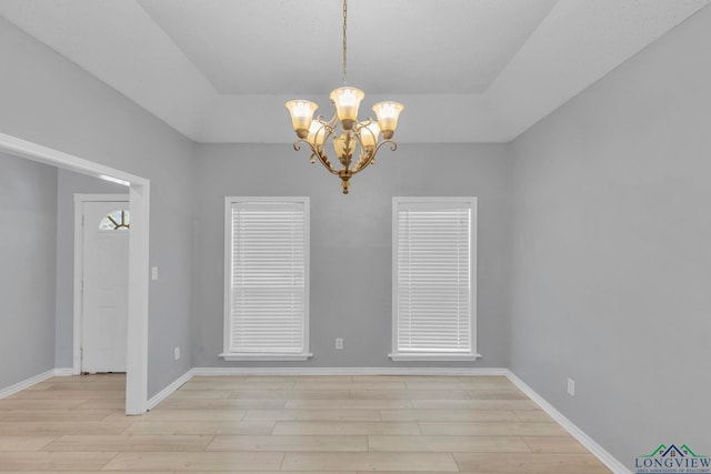 unfurnished dining area with a tray ceiling, light wood-type flooring, and baseboards