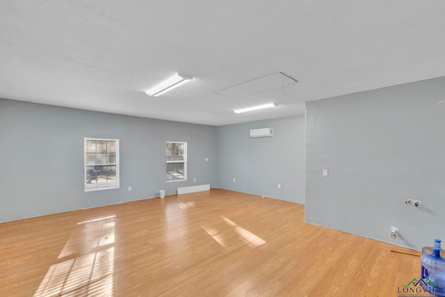 unfurnished room featuring a wall unit AC, light wood-style flooring, and a textured ceiling