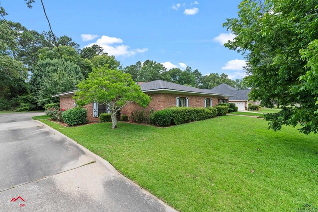 825 University Dr, Carthage, TX 75633 - view of home's exterior featuring an attached garage, a yard, brick siding, and driveway