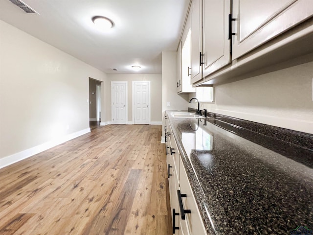 kitchen with white cabinets, light hardwood / wood-style floors, sink, and dark stone counters