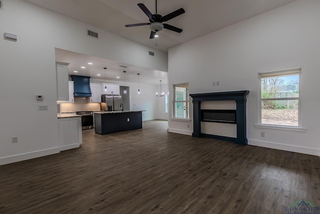 unfurnished living room with ceiling fan with notable chandelier, high vaulted ceiling, and dark hardwood / wood-style floors