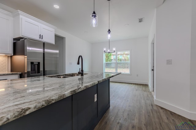 kitchen featuring stainless steel refrigerator with ice dispenser, sink, light stone counters, pendant lighting, and white cabinets