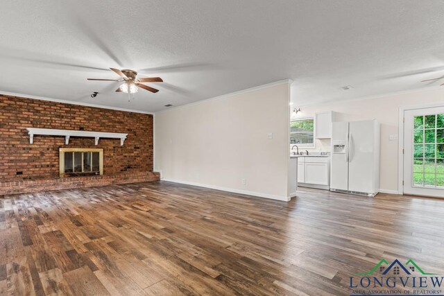 11562 19th Ave, Tyler, TX 75709 - unfurnished living room with a ceiling fan, wood finished floors, a fireplace, a sink, and crown molding