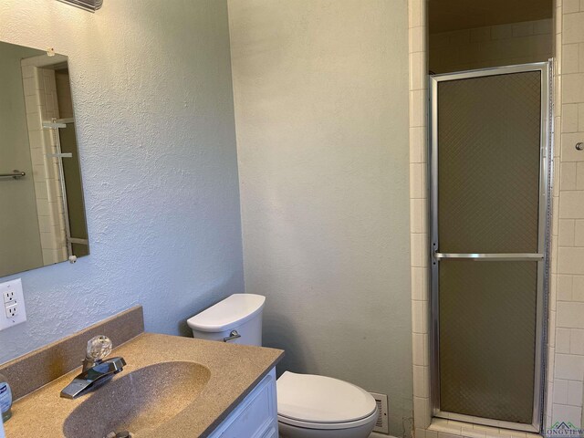 bathroom with vanity, toilet, a shower stall, and a textured wall