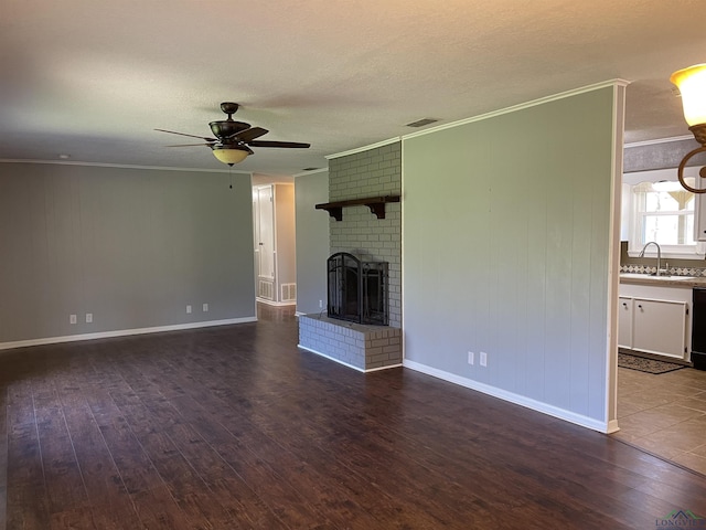 unfurnished living room with visible vents, a sink, dark wood finished floors, a fireplace, and crown molding