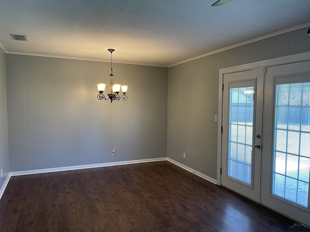 empty room featuring french doors, dark wood finished floors, ornamental molding, and a chandelier