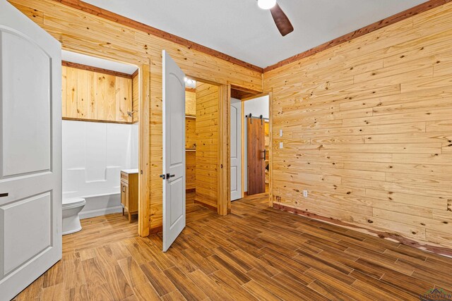 unfurnished bedroom with hardwood / wood-style floors, ensuite bath, wooden walls, and ceiling fan