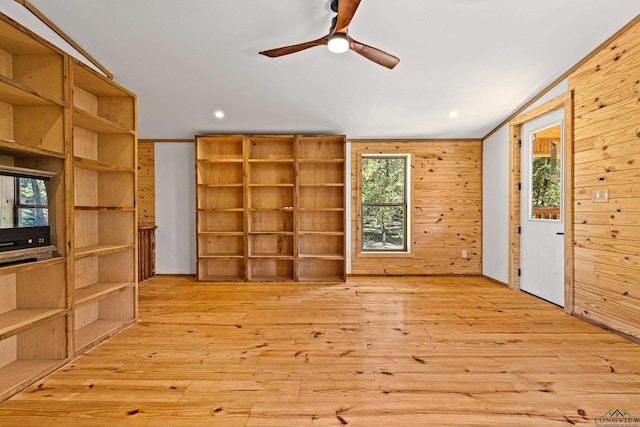 unfurnished living room with a healthy amount of sunlight, wooden walls, and light hardwood / wood-style flooring